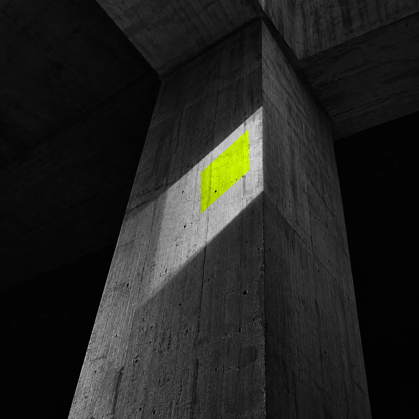 Sunlight falling across angled concrete walls, with a small square of fluoro-yellow light.