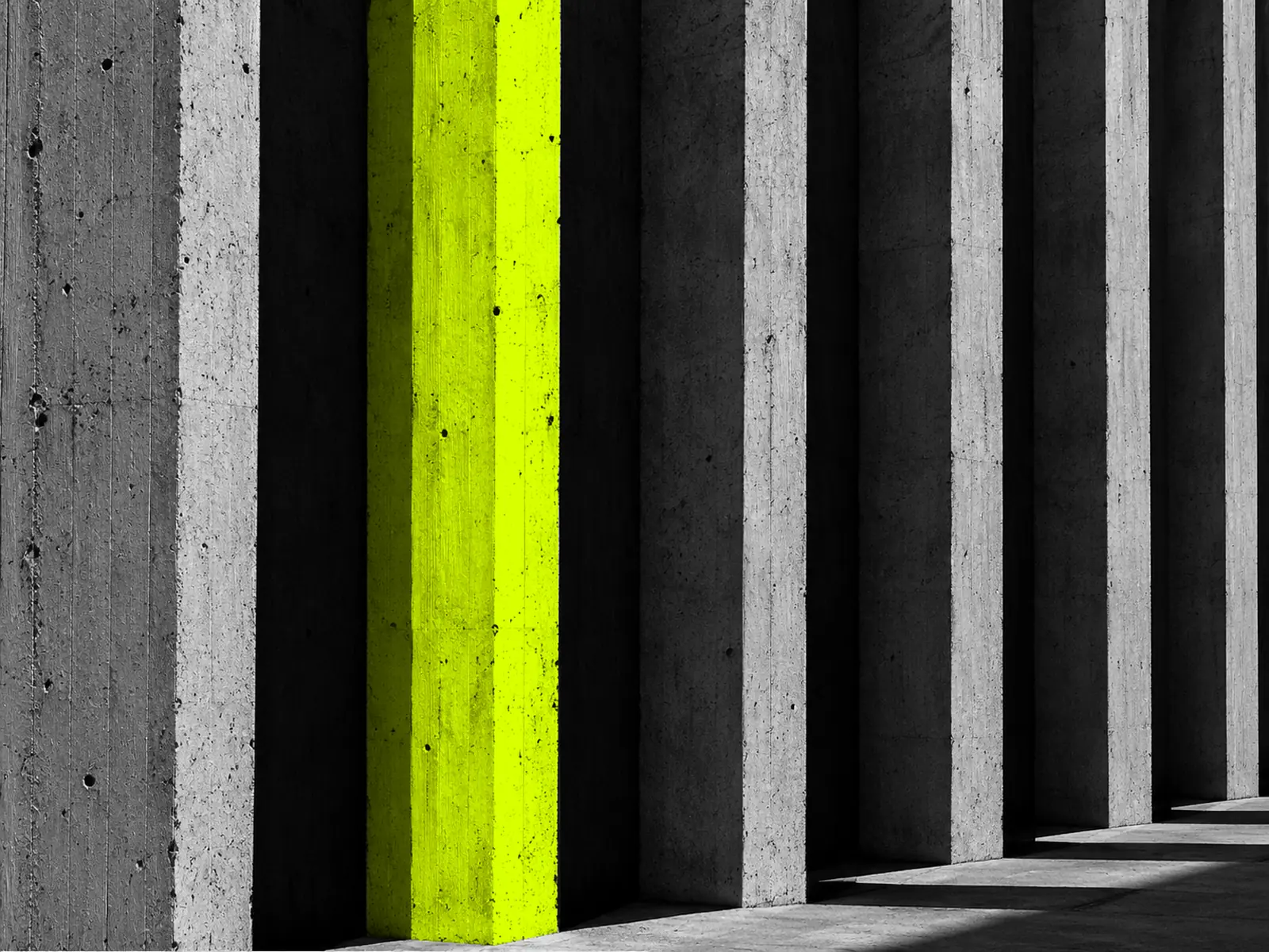 Tall concrete columns in a row, one lit fluoro yellow, casting long shadows.