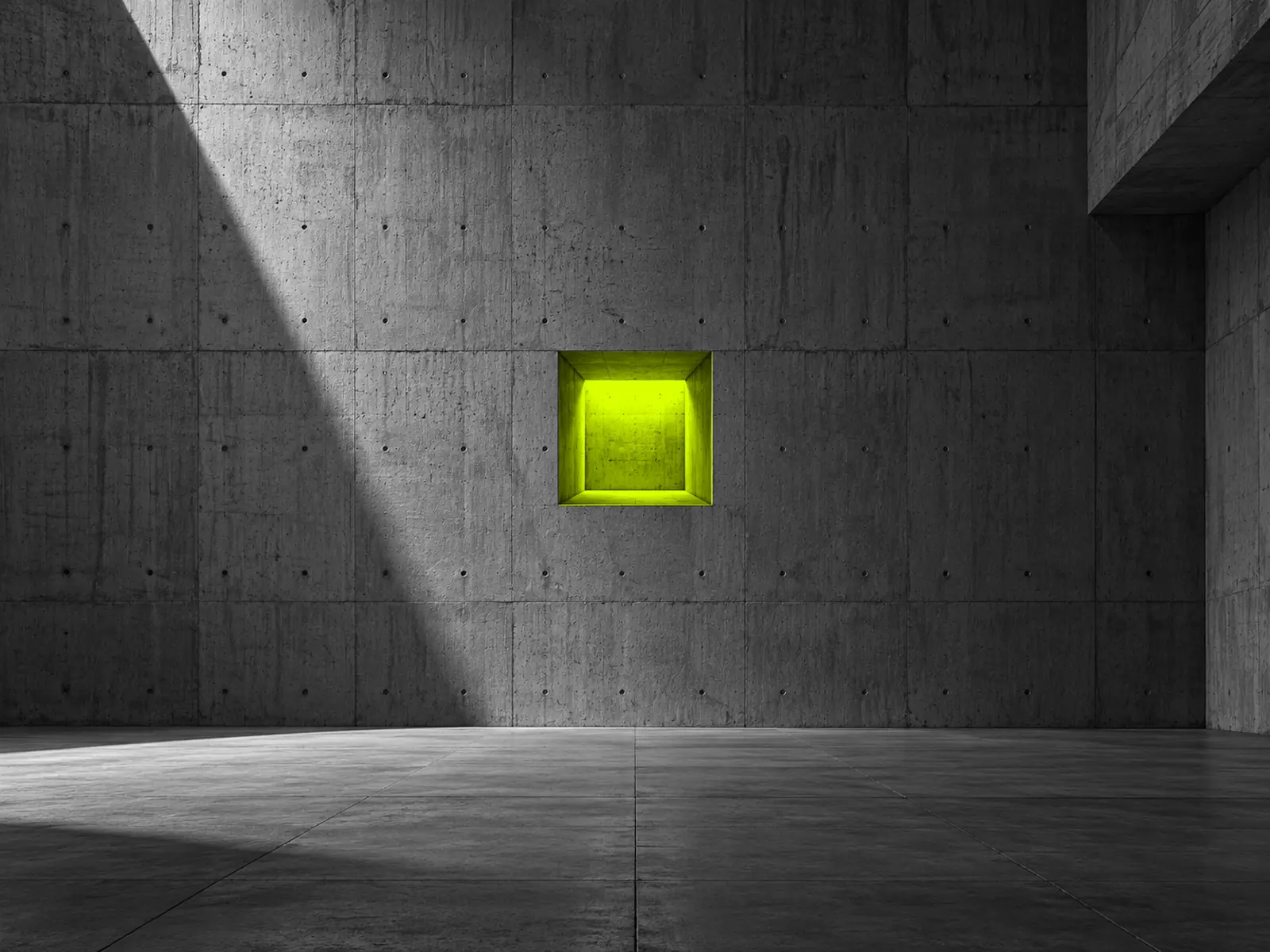 A massive concrete wall with a deep square recess glowing fluoro yellow from inside.