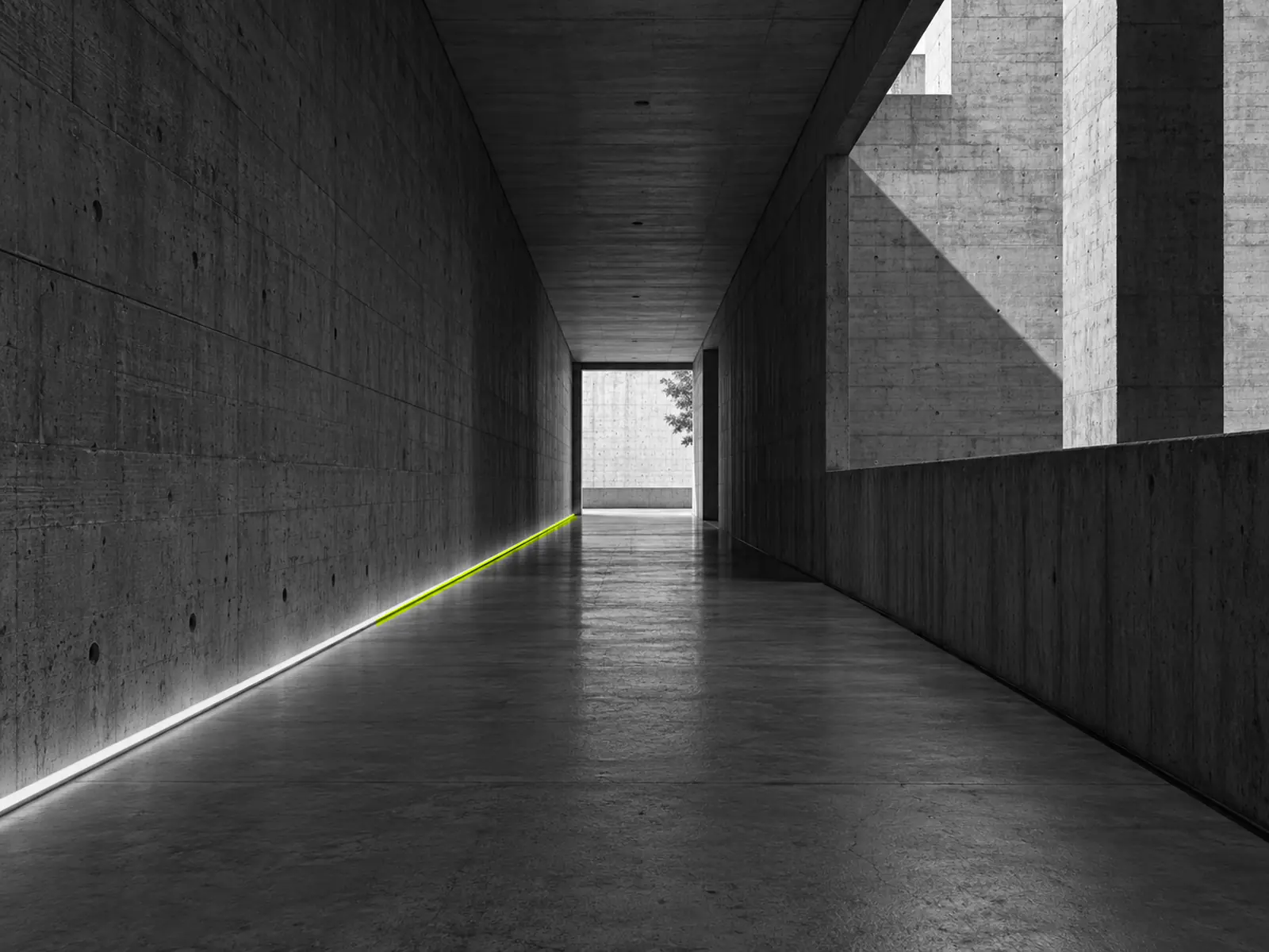 A long concrete corridor with a thin line of fluoro-yellow light along the floor, leading to a bright opening.