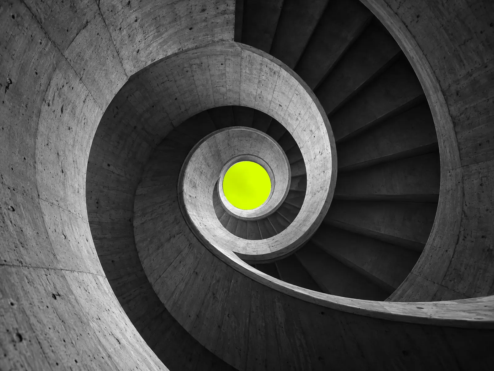 Looking up a spiral concrete staircase to a small round opening lit fluoro yellow.