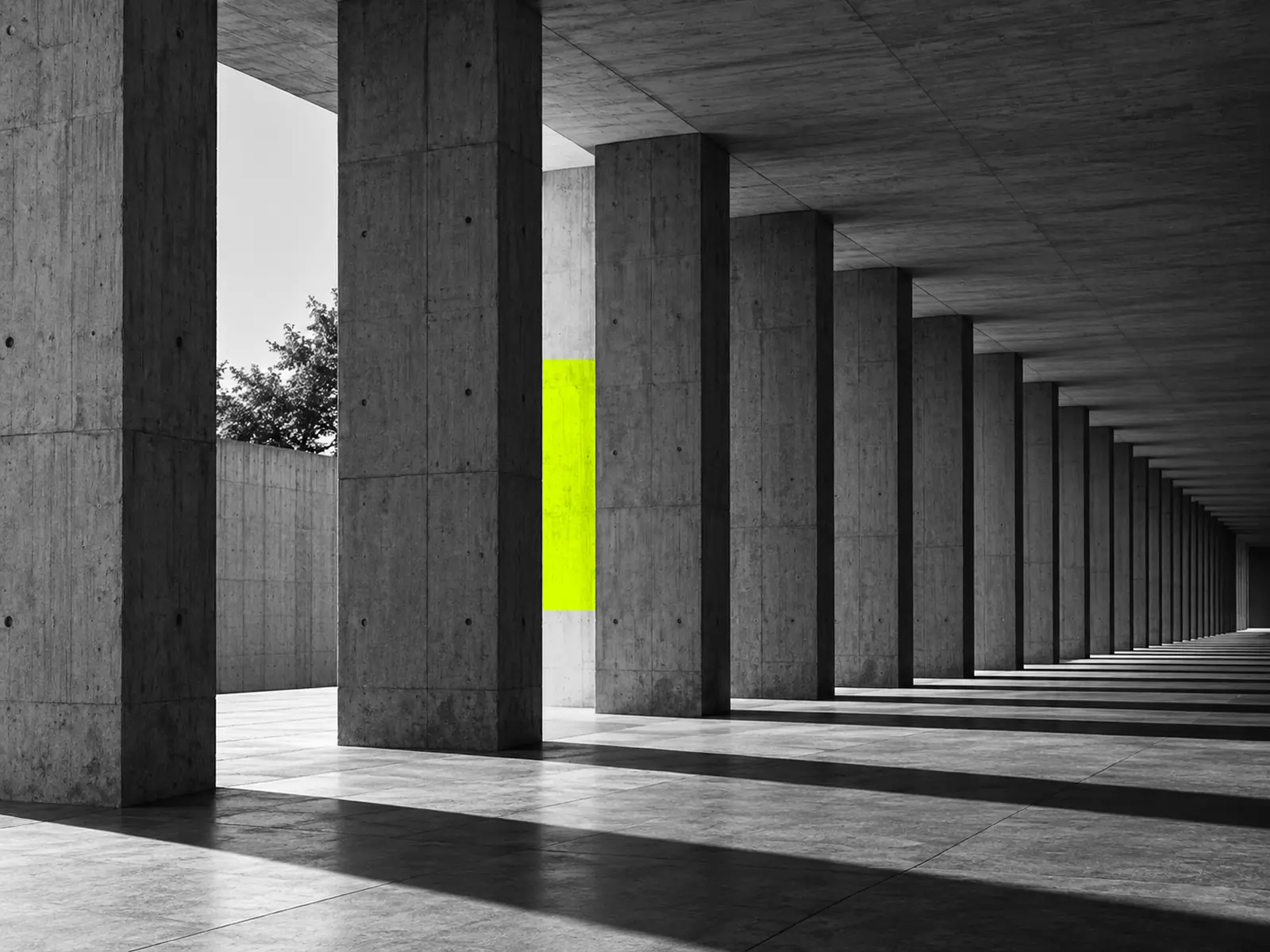 A long concrete colonnade of identical columns, with fluoro-yellow light between one pair.