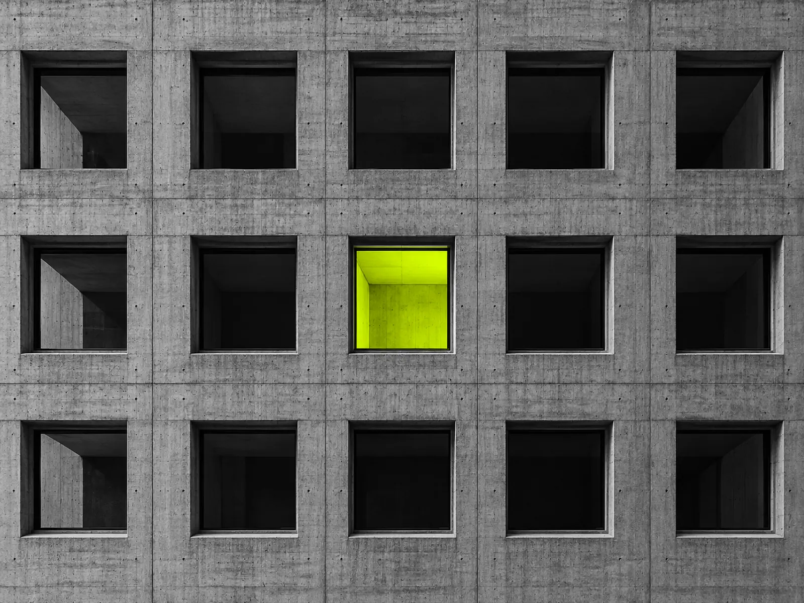 A concrete facade with a grid of identical square windows, one glowing fluoro yellow.