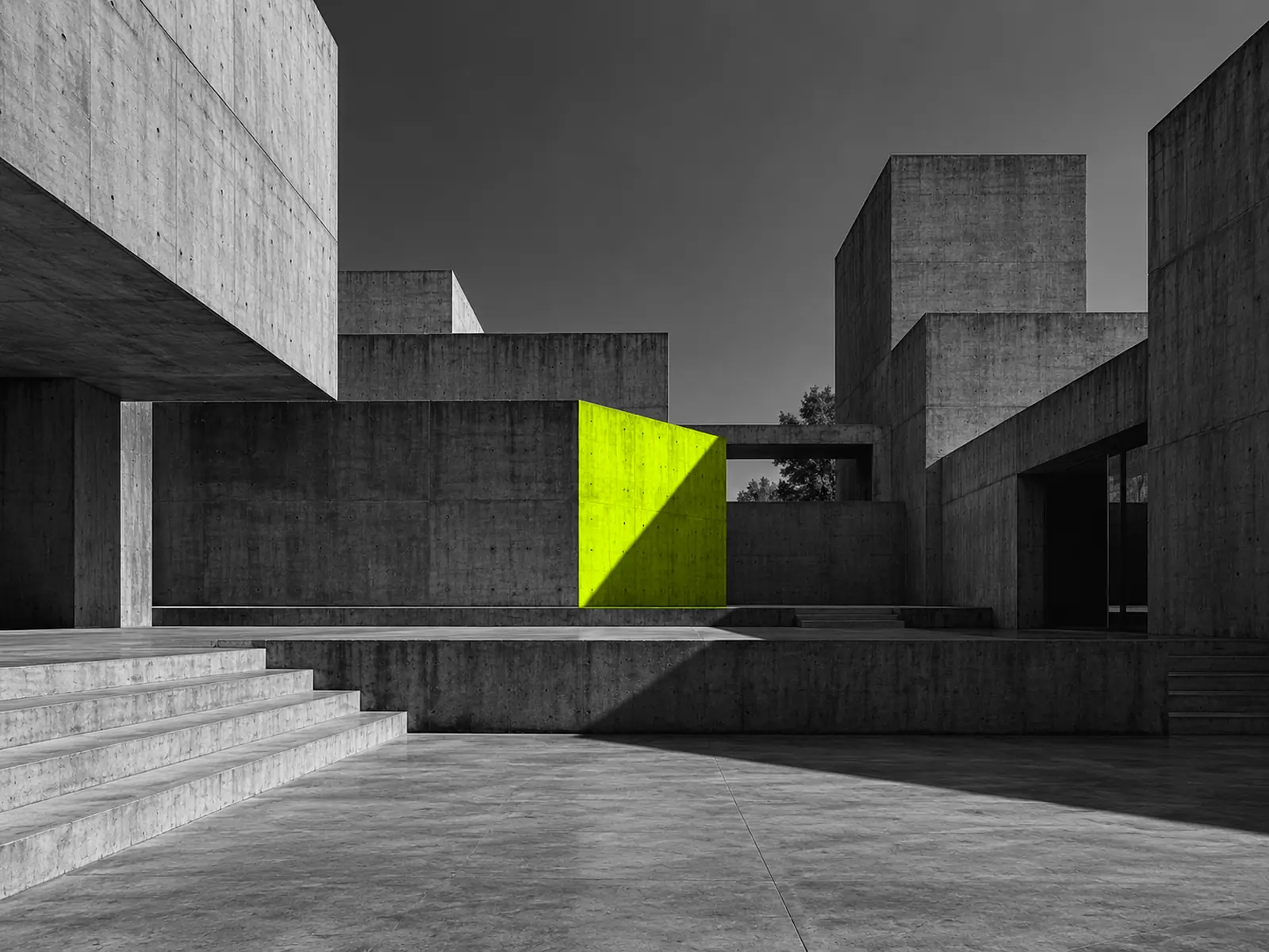 A brutalist courtyard of geometric concrete volumes at different heights, with one face lit fluoro yellow.